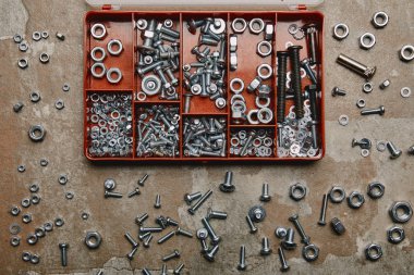 Top view of box with bolts and scattered nails and screws on old background  clipart
