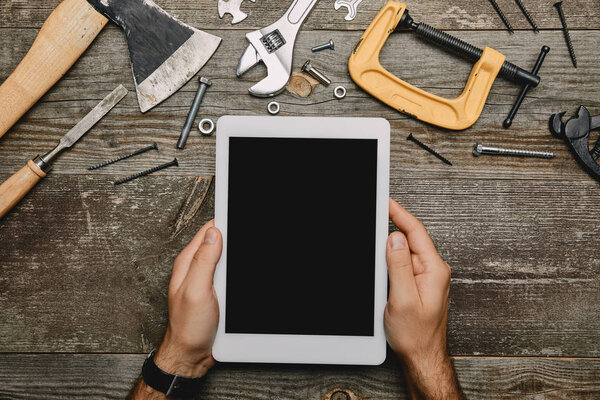 Partial view of worker using digital tablet in workshop with different carpentry tools 