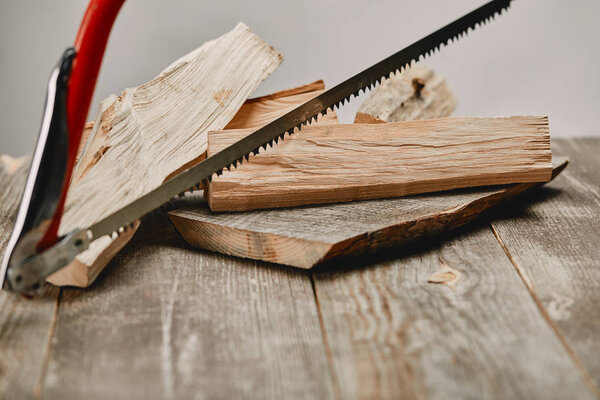 Close up view of hacksaw and wood logs on wooden table on grey background
