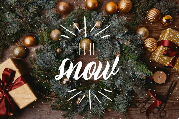 top view of Christmas gift boxes and fir wreath on wooden table with "let it snow" lettering and snow