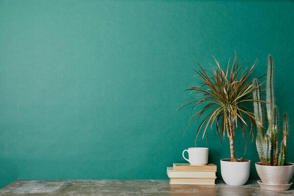 Cup of coffee on books and plants in flowerpots on green background