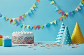 leckere Geburtstagstorte, Geschenke, Partyhüte und Konfetti auf blauem Hintergrund mit Fahnenmeer