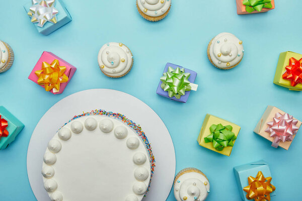 Top view of delicious cake, cupcakes and gifts on blue background