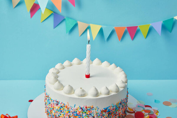 Candle on birthday cake with sugar sprinkles on blue background with bunting
