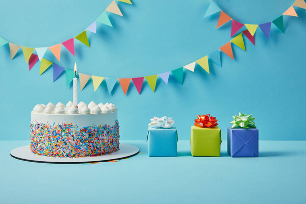 Tasty cake with sugar sprinkles and gifts on blue background with colorful bunting