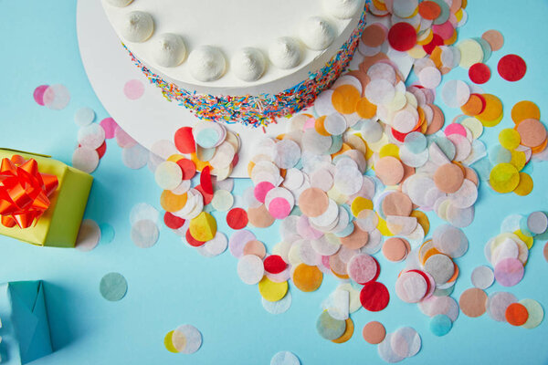 Top view of delicious cake, gifts and confetti on blue background