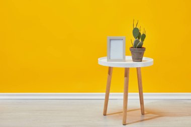 Cactus in flowerpot and empty photo frame on coffee table clipart