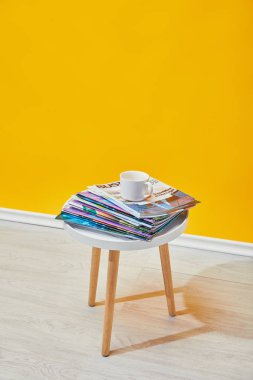 coffee table with journals and white cup near yellow wall clipart