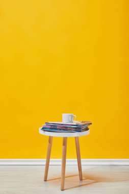 Little coffee table with journals and cup of coffee near yellow wall  clipart