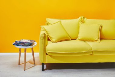 Sofa with pillows and coffee table with press near yellow wall clipart