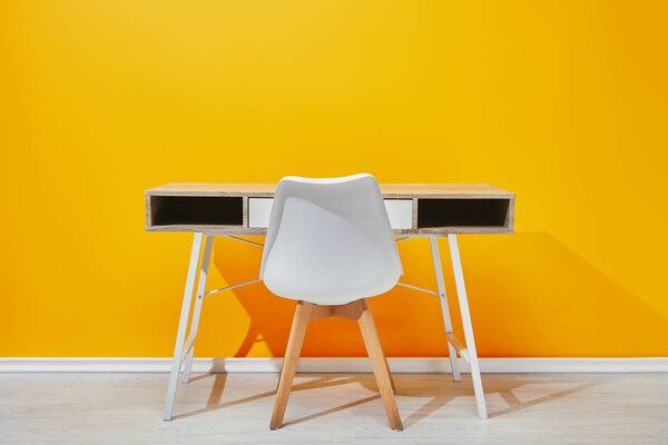 minimalistic wooden table with chair with yellow wall at background