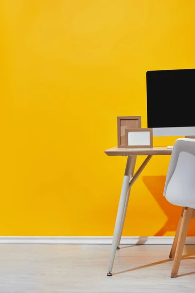 コンピューターと黄色の壁の近くの職場で空のフォト フレーム — ストック写真