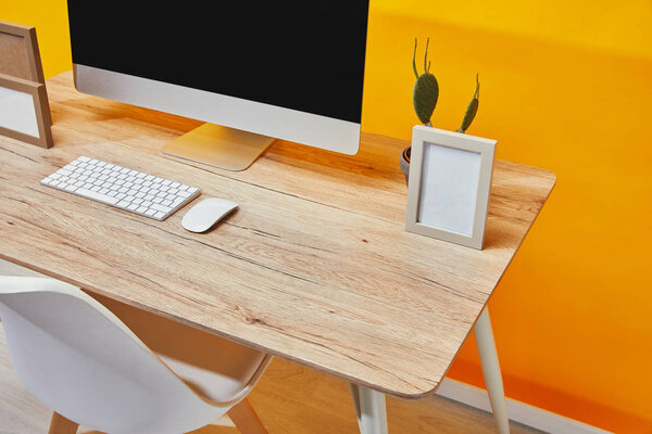 Computer, empty photo frames and cactus in flowerpot at wooden table 