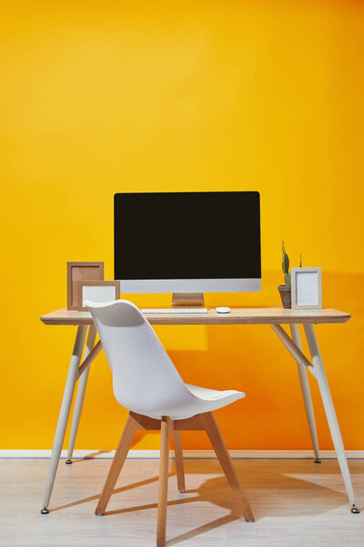 Computer, photo frames and cactus on workplace with yellow wall at background