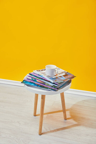coffee table with journals and white cup near yellow wall