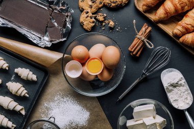 Tepsi hamur kruvasan, malzemeler ve çırpma teli ile yükseltilmiş görünümü siyah masada