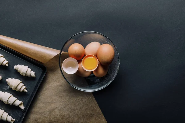 鸡蛋在碗和托盘与面团在黑色桌子上的羊角面包的高视图 — 免费的图库照片