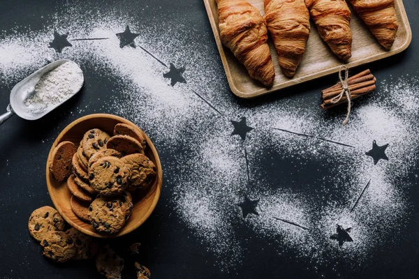 flat lay with croissants and cookies on table covered by flour with stars as big dipper constellation