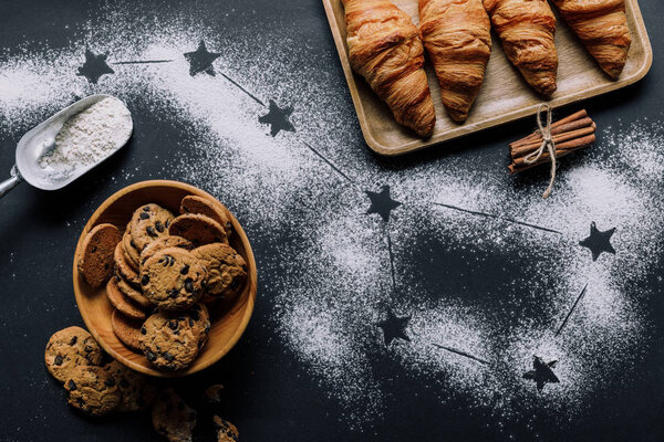 flat lay with croissants and cookies on table covered by flour with stars as big dipper constellation 