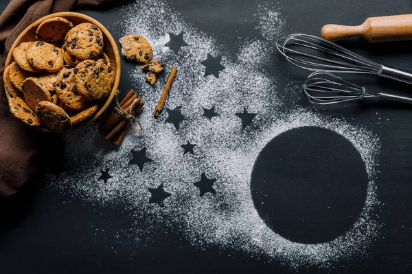 view from above of cookies in bowl, whisks and rolling pin on table covered by flour with symbol of stars