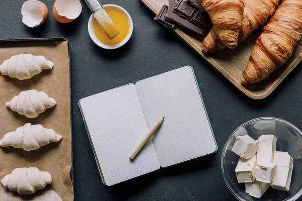 クロワッサンやテーブルに食材の生地に囲まれた空白の教科書の平面図  — 無料ストックフォト