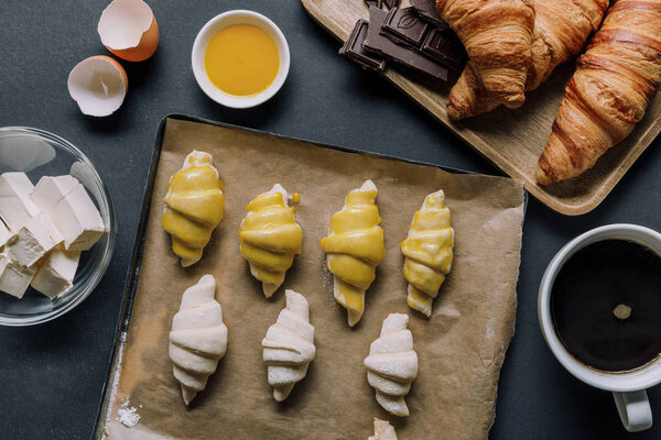 top view of tray with dough for croissants, ingredients and coffee cup on black table