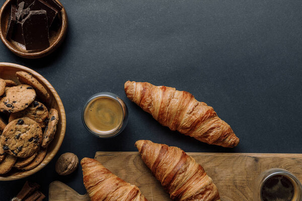 flat lay with walnut, coffee, croissants, chocolate and cookies on black table