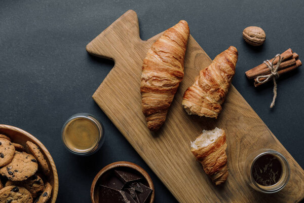 elevated view of cinnamon, coffee, croissants, chocolate and cookies on black table