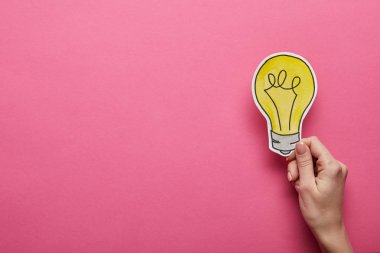 top view of hand holding yellow light bulb on pink background clipart