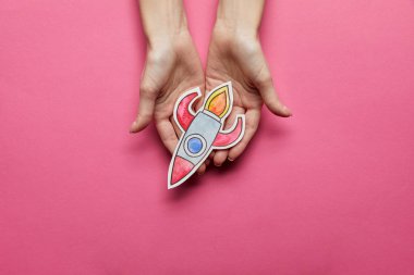top view of hands holding rocket on pink background clipart