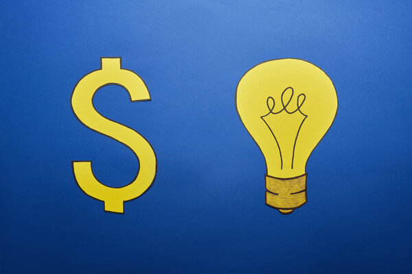 top view of yellow paper light bulb and dollar sign on blue background