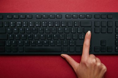 Kadın kırmızı bir arka plan üzerinde siyah bilgisayar klavyesindeki düğmeye üstten görünüm 
