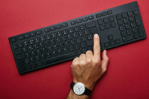 赤の背景に黒のコンピューター キーボード ボタンを押す男性の手の上から見る — ストック写真