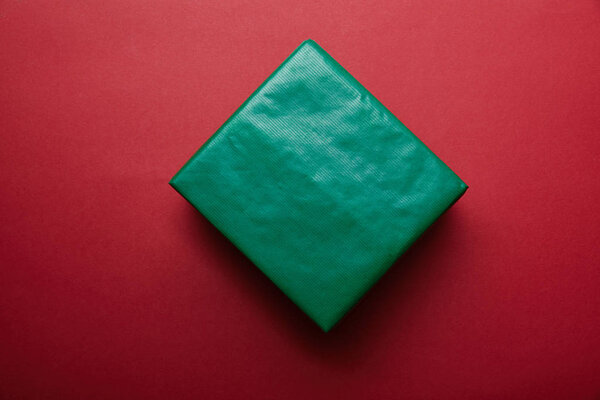 Вид сверху подарка, завернутого в зеленую оберточную бумагу на красном фоне
 