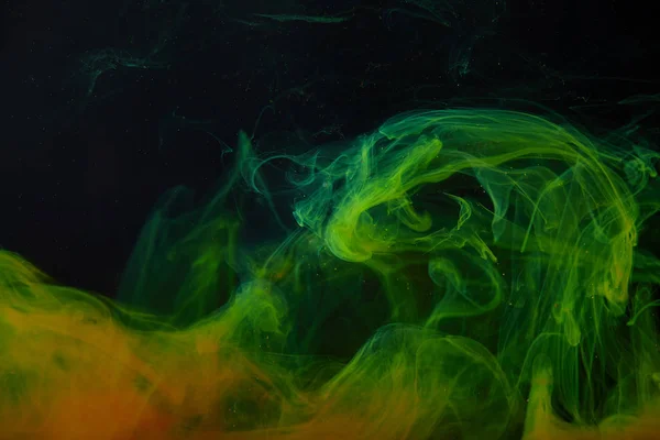 暗い背景と塗料の抽象的な緑とオレンジ色の渦巻き  — 無料ストックフォト