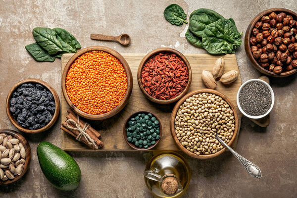 верхний вид деревянной доски с бобовыми, ягодами годжи и здоровыми ингредиентами на деревенском фоне
