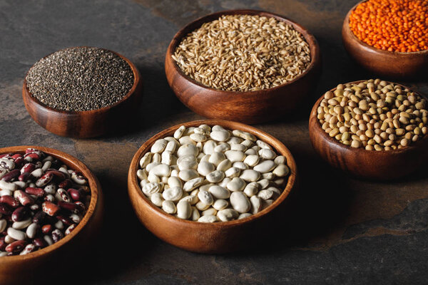 variety of beans, chia seeds and oat groats in wooden bowls on table