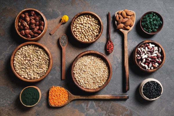 flat lay of wooden bowls and spoons with superfoods, legumes and grains on table