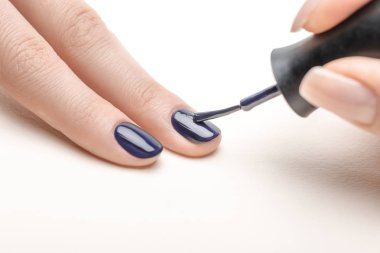 female manicurist applying navy blue nail polish on fingernail of woman on white background clipart