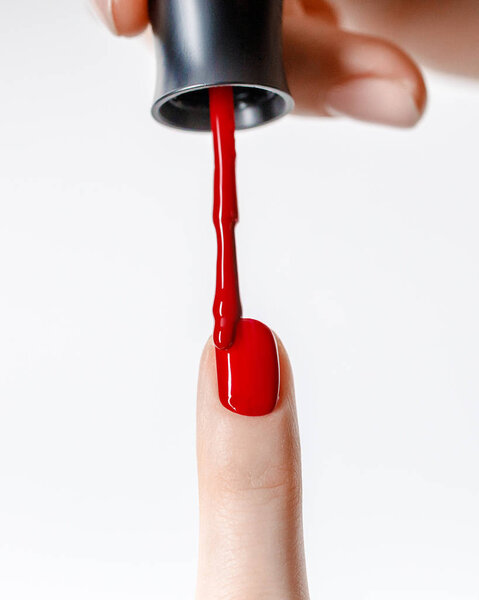cropped view of woman applying red nail polish on fingernail isolated on white