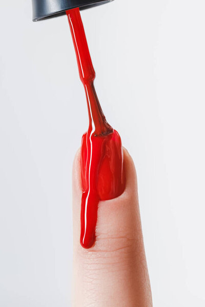 partial view of woman applying dripping red nail polish on fingernail isolated on grey