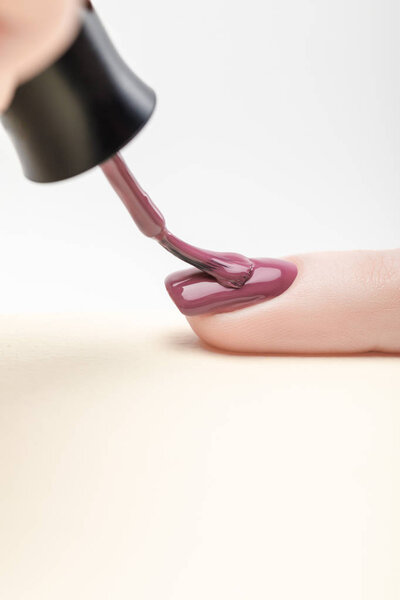 manicurist applying purple nail polish on fingernail of woman on grey background
