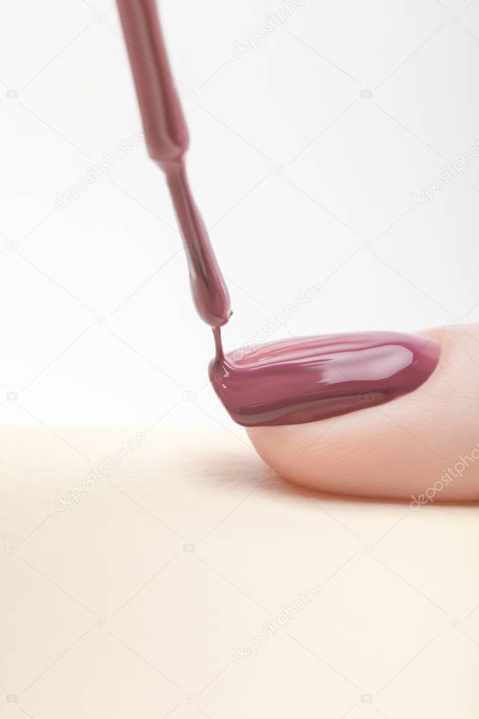 purple nail polish on fingernail of woman with wet brush on grey background
