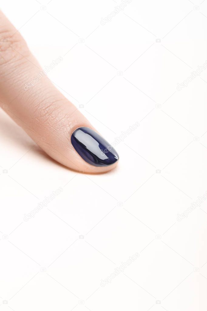 fingernail with shiny navy blue nail polish on white background