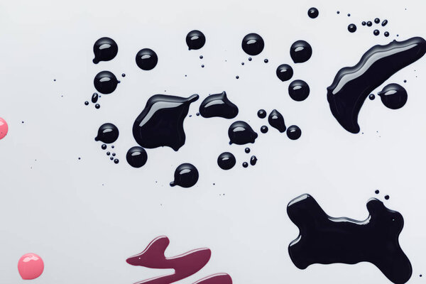 верхний вид влажных черных разливов лака для ногтей вблизи розовых капель, изолированных на сером
