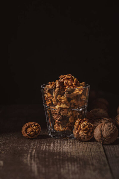 close up view of shelled walnuts in glass on wooden tabletop on black background
