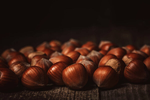 close up view of hazelnuts on wooden surface on black background