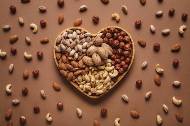 flat lay with heart shaped box with different nuts assortment on brown tabletop clipart