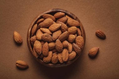 top view of in wooden bowl almonds on brown background clipart