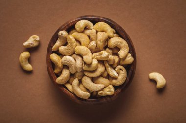top view of cashew nuts in wooden bowl on brown background clipart